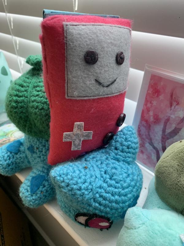 A photograph of Ferretsroq’s crochet Bulbasaur with a felt Game Boy Color, gifts from his friends that mean an awful lot to him